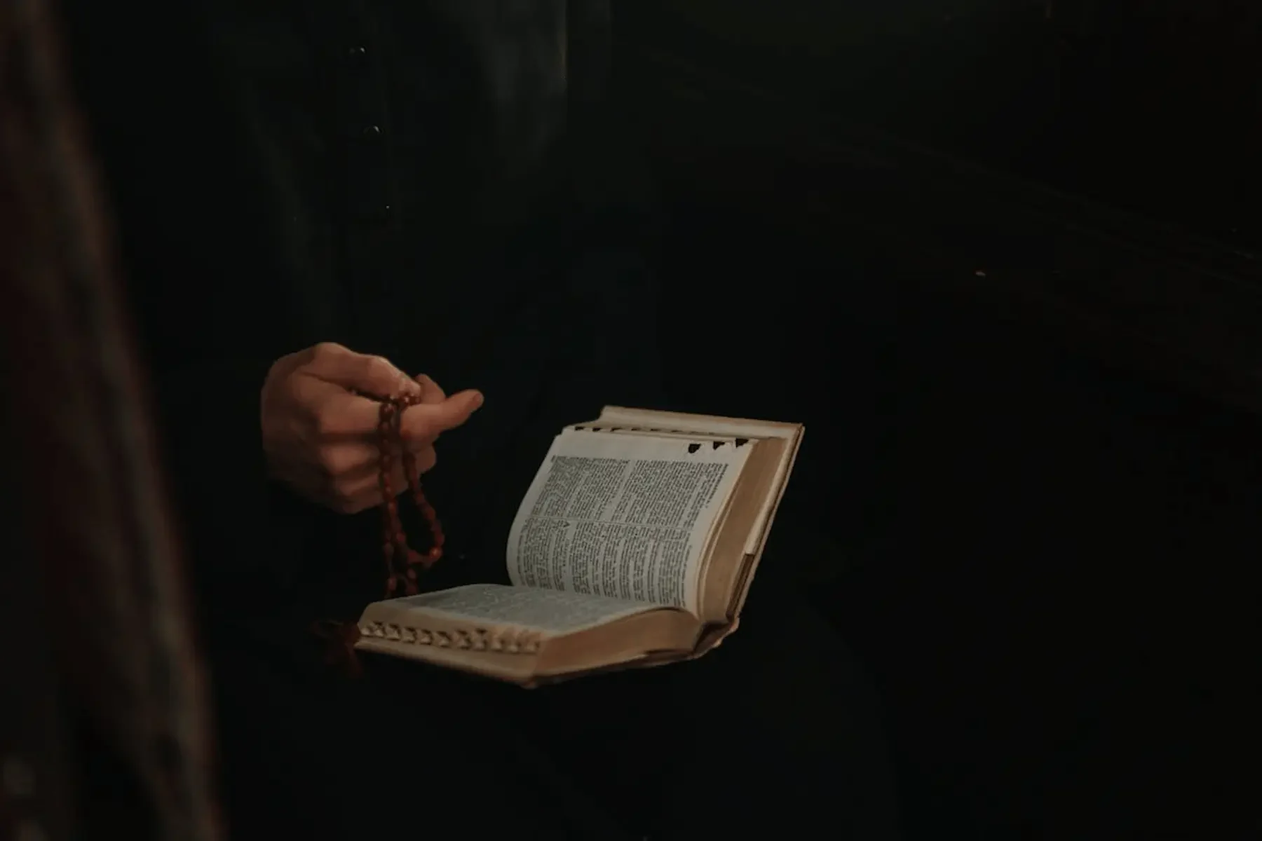 padre con rosario en mano y una biblia