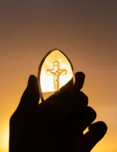 unas manos frente al sol aguantando una piedra con la imagen de Jesús en la cruz